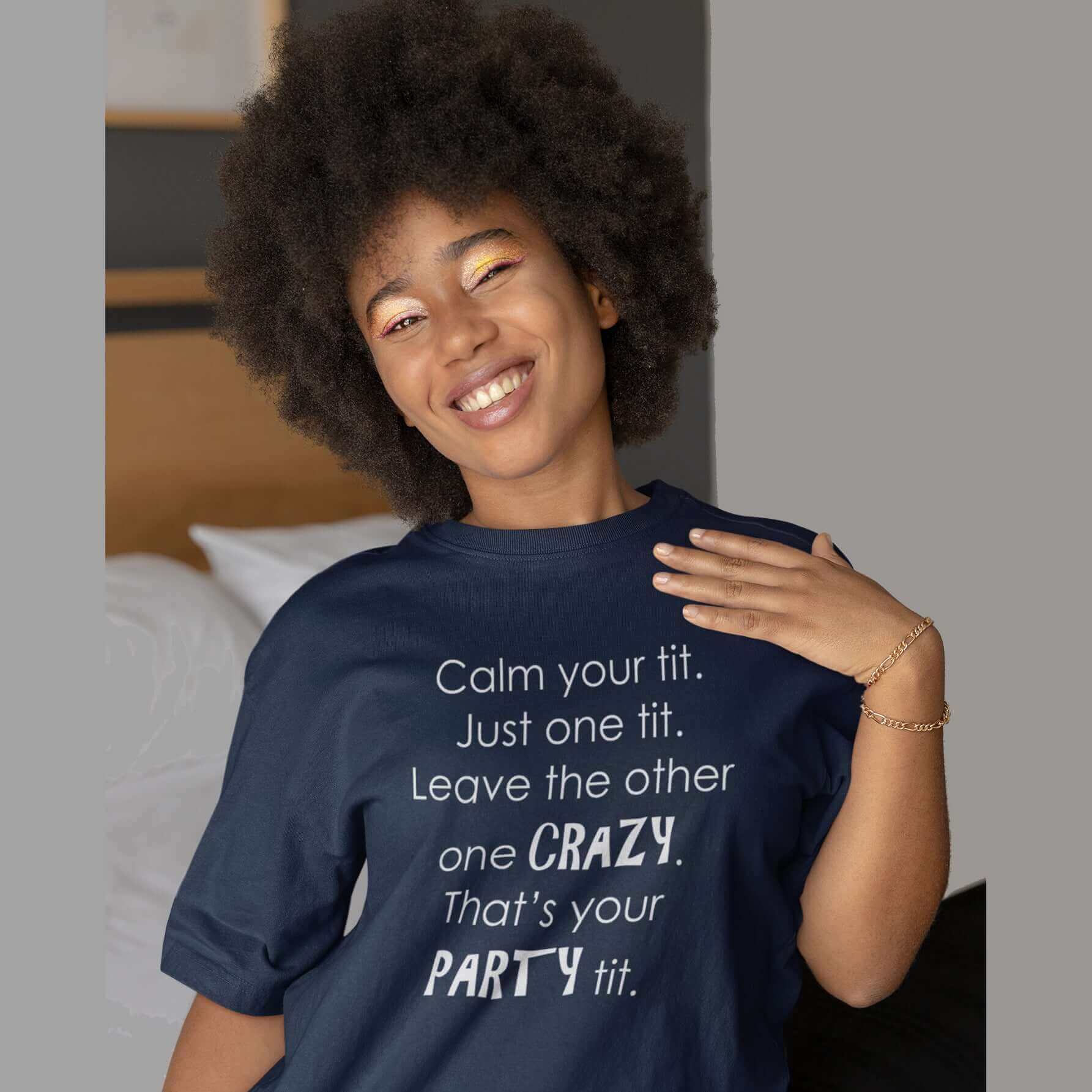 Woman wearing a navy blue t-shirt with the funny phrase Calm your tit, just one tit. Leave the other one crazy, that's your party tit printed on the front.