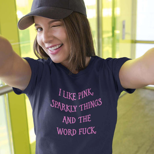 Woman wearing a navy blue t-shirt with the phrase I like pink, sparkly things and the word fuck printed in pink on the front of the shirt.