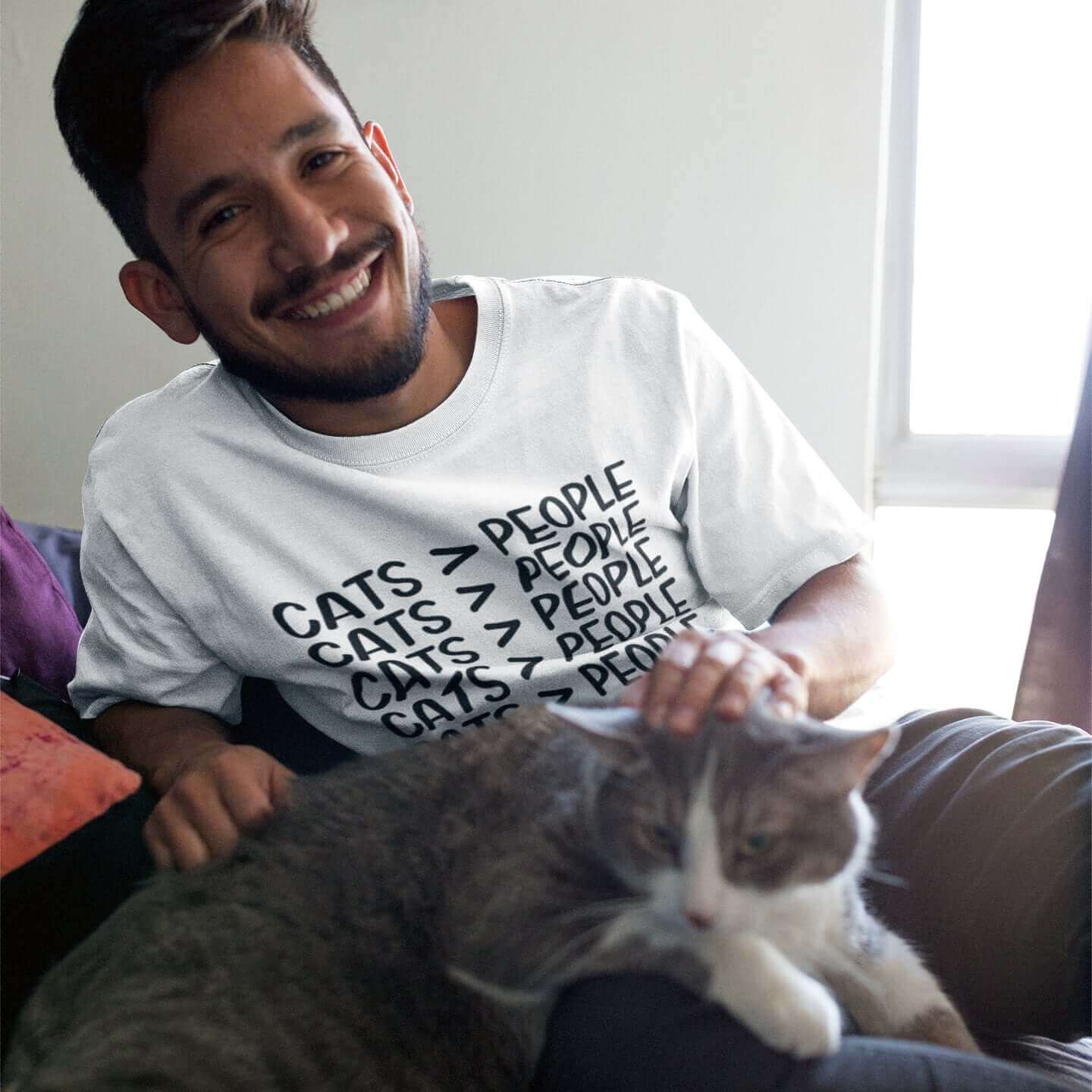 Man petting a cat while wearing a white t-shirt with the words Cats > people printed on the front.