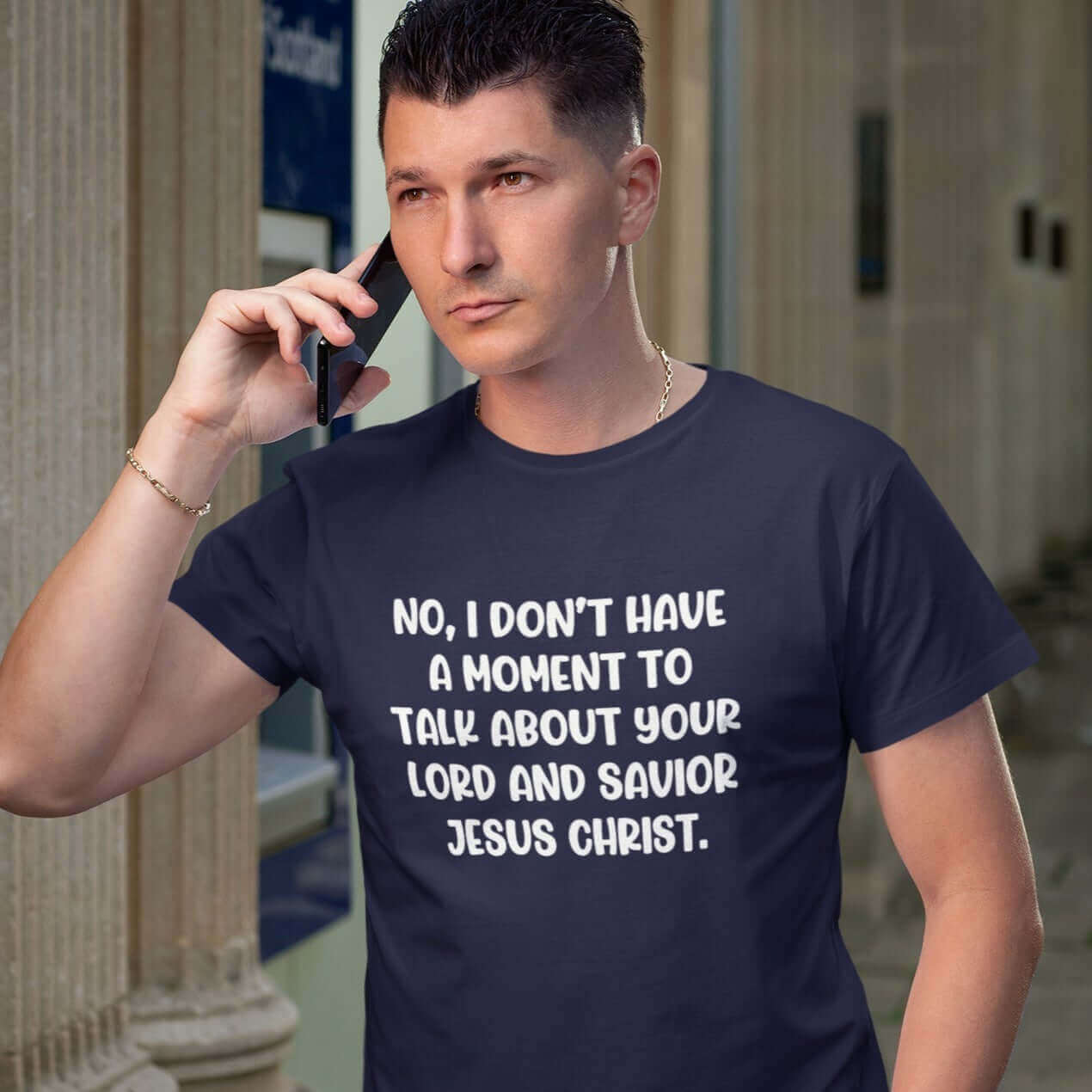 Man on a cell phone wearing a navy blue t-shirt with the phrase No, I don't have a moment to talk about your lord and savior Jesus Christ printed on the front.
