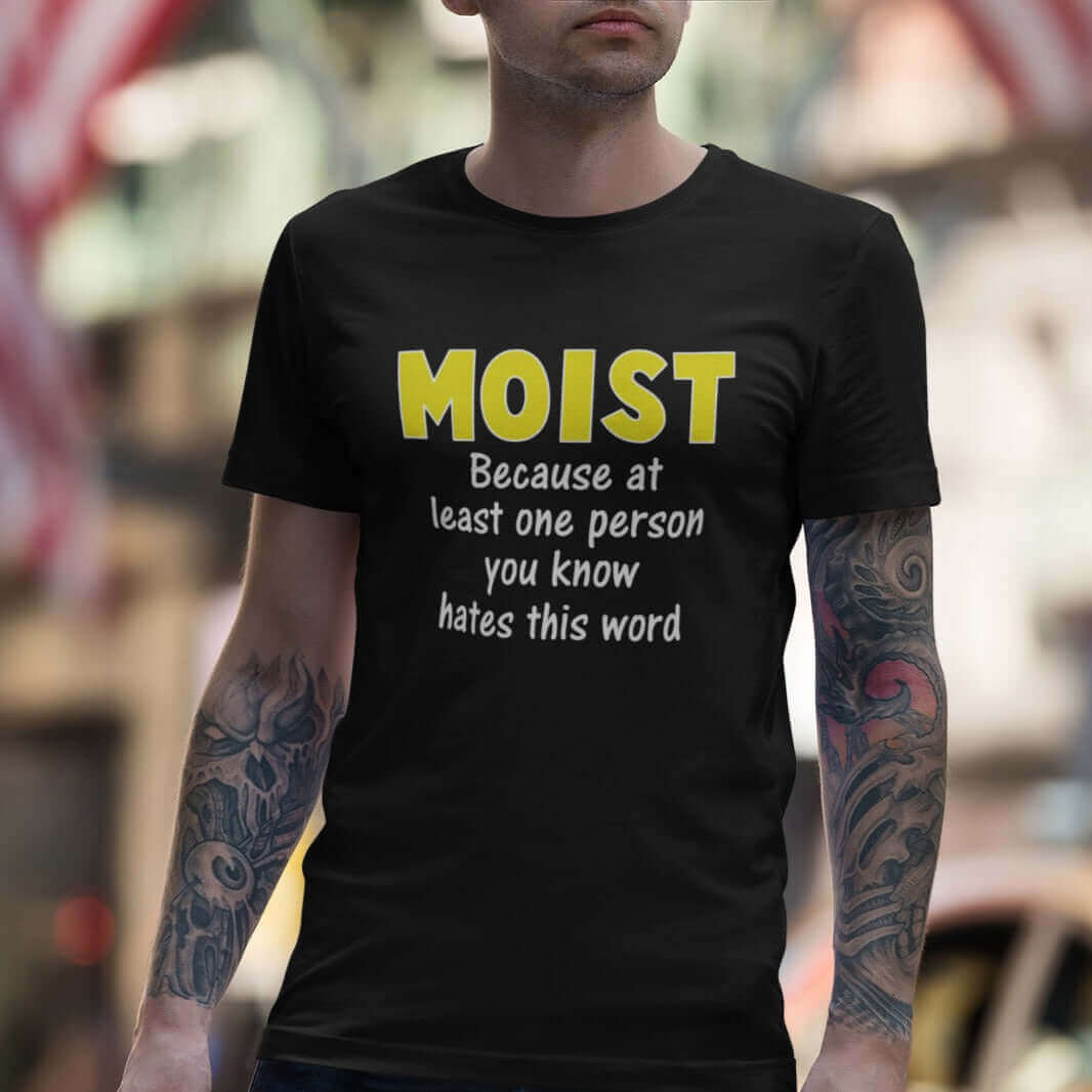 Tattooed man wearing black t-shirt with the word Moist printed in large yellow bold font. In smaller font under the word moist is the phrase Because at least one person you know hates this word. 