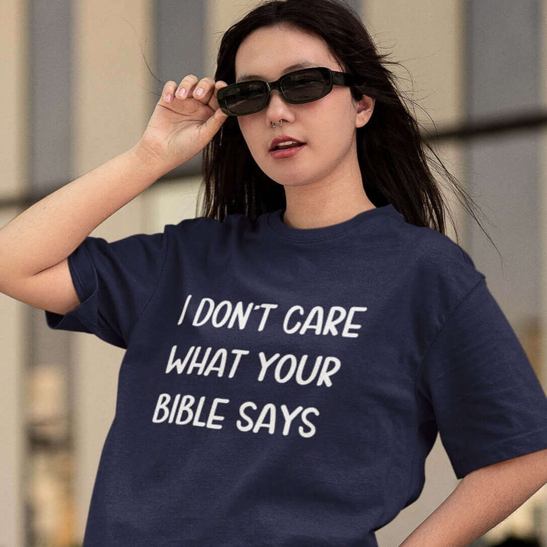 Woman wearing sunglasses and a navy blue t-shirt with the words I don't care what your bible says printed on the front.