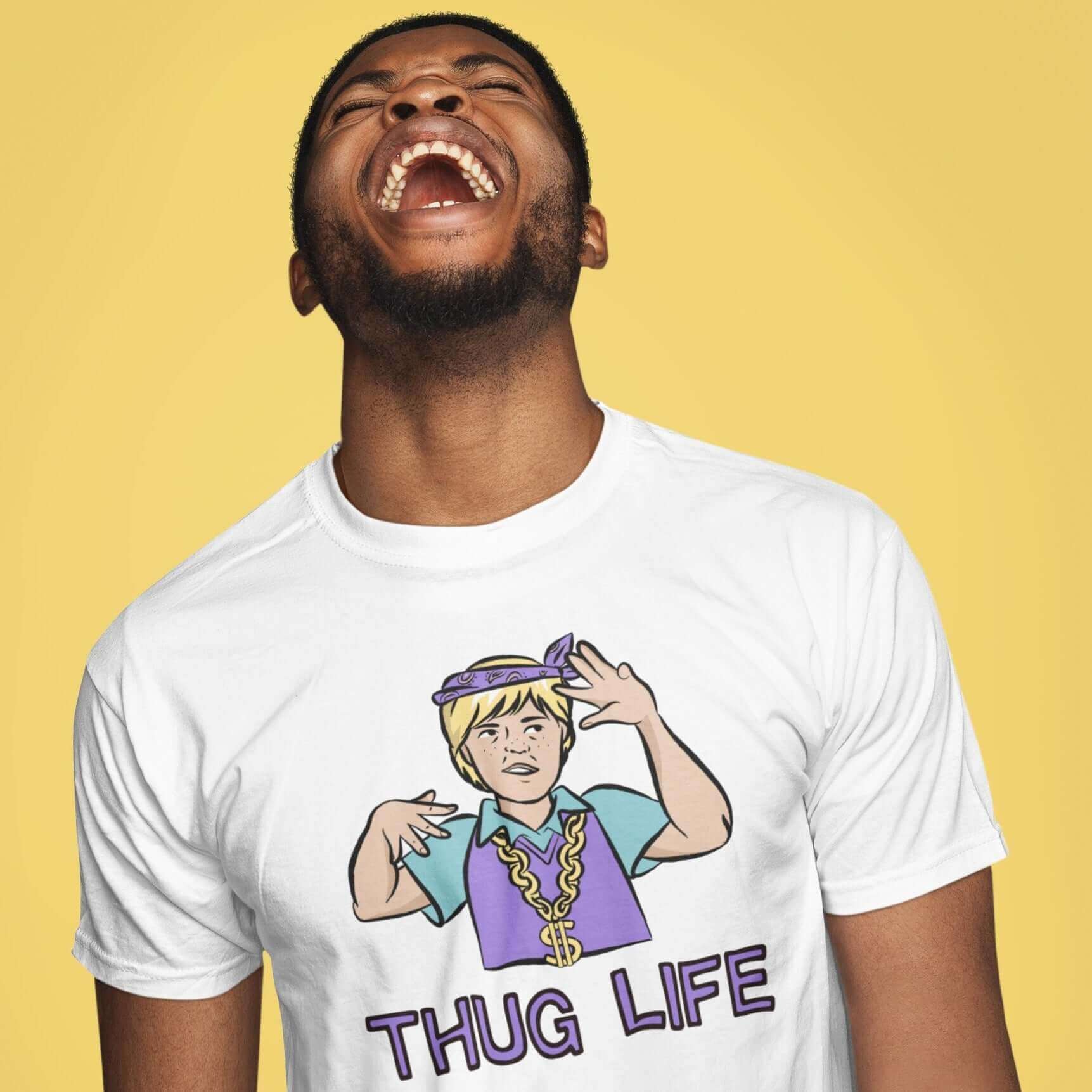 Laughing man wearing white t-shirt with a parody image of a blond haired child trying to be a gangster with the words Thug Life printed on the front.