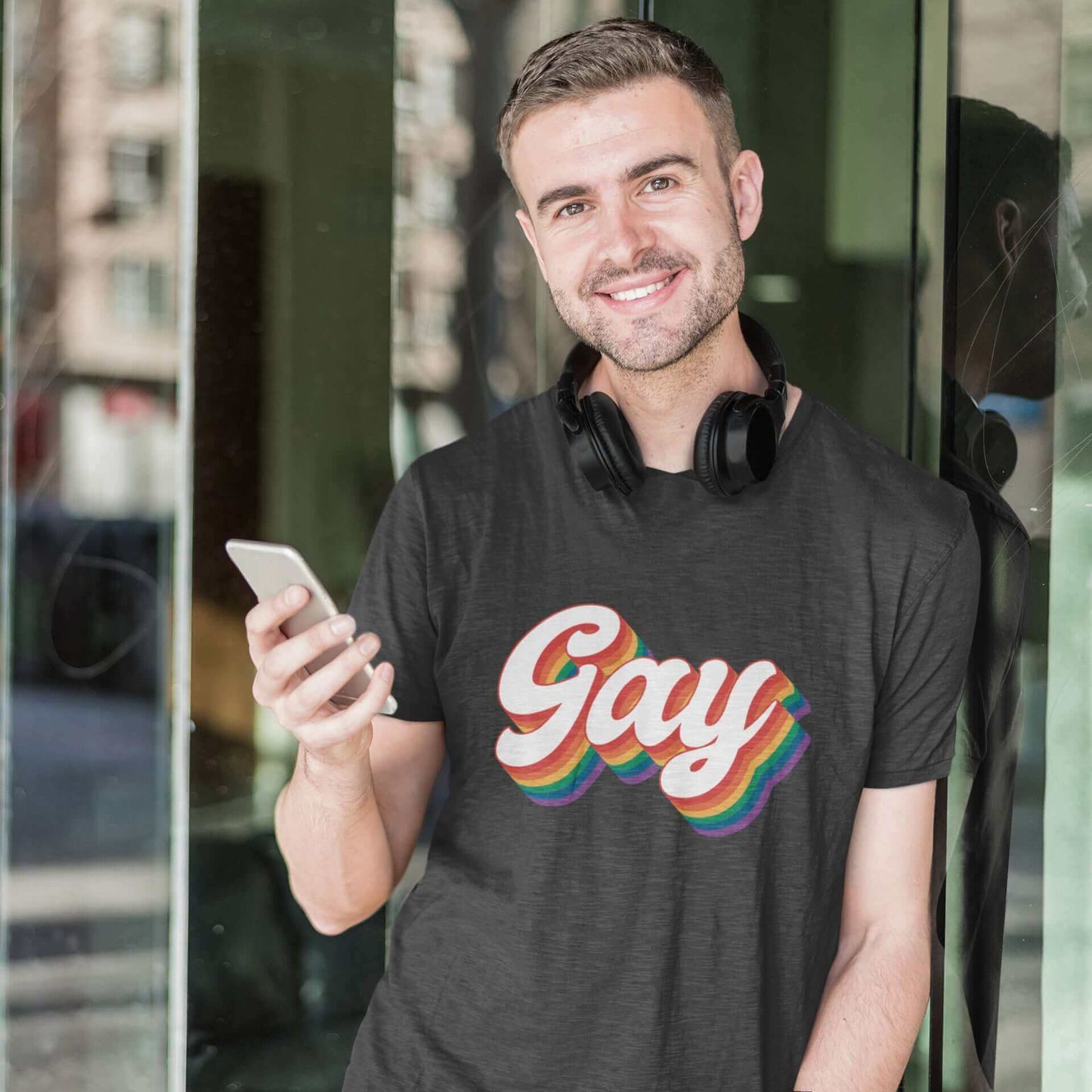Man wearing dark heather grey t-shirt with the word Gay printed on the front. The word gay is outlined in rainbow.