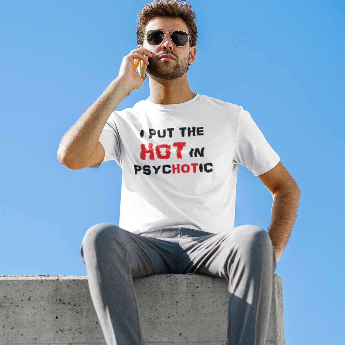 Man talking on cell phone wearing a white t-shirt has the words I put the hot in psychotic printed on the front.