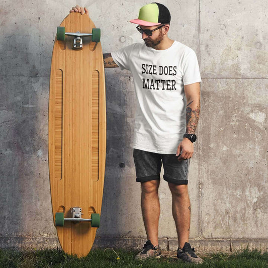 Man standing next to a very long skateboard wearing a white t-shirt with the words size does matter printed on the front.