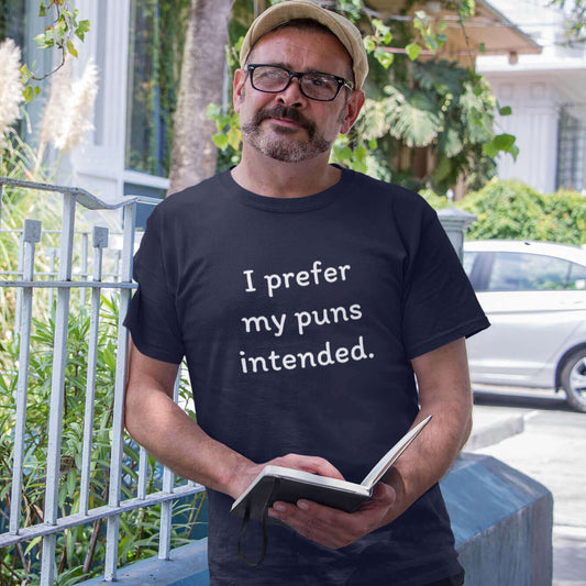 Man reading a book while wearing a navy blue t-shirt with the phrase I prefer my puns intended printed on the front.