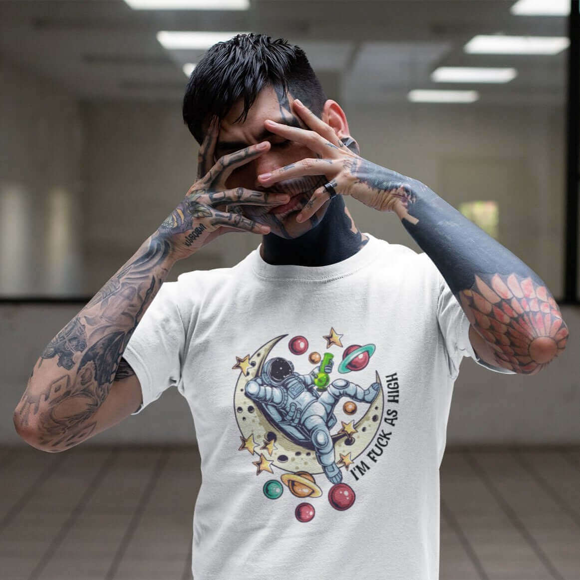 Tattooed man wearing a white t-shirt with graphic of an astronaut sitting on the moon while smoking a bong with the words I'm fuck as high printed on the front.