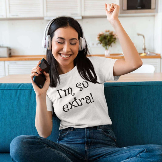 Woman sitting in a sofa cheering while wearing a white t-shirt with the words I'm so extra printed on the front.