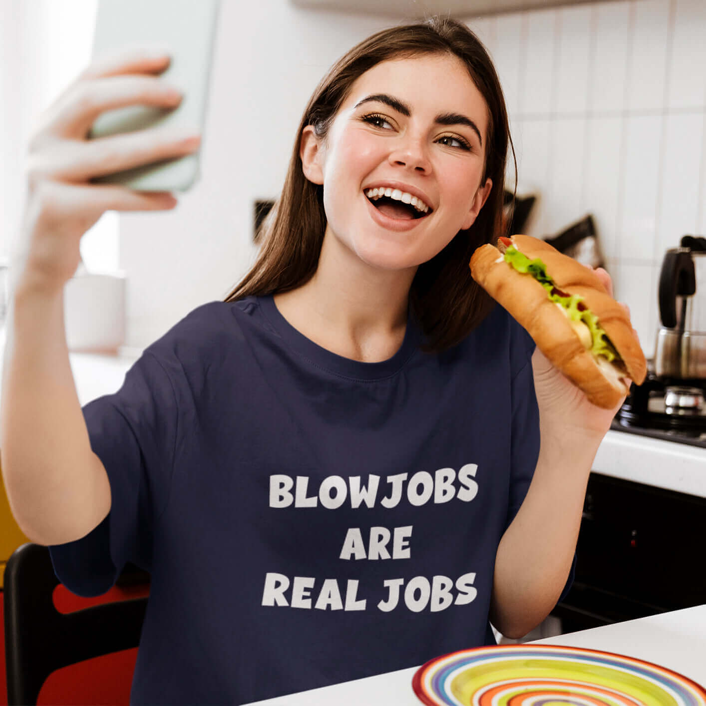 Woman holding a sub sandwich and wearing a navy blue t-shirt with the words Blowjobs are real jobs printed on the front.