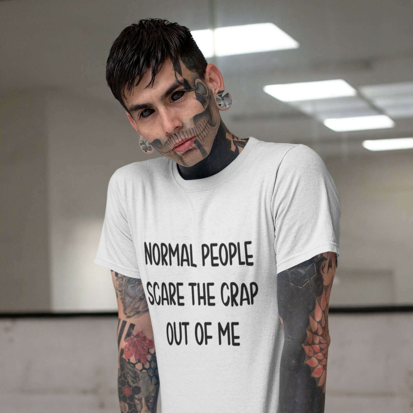 Heavily tattooed man wearing white t-shirt with the phrase Normal people scare the crap out of me printed on the front.