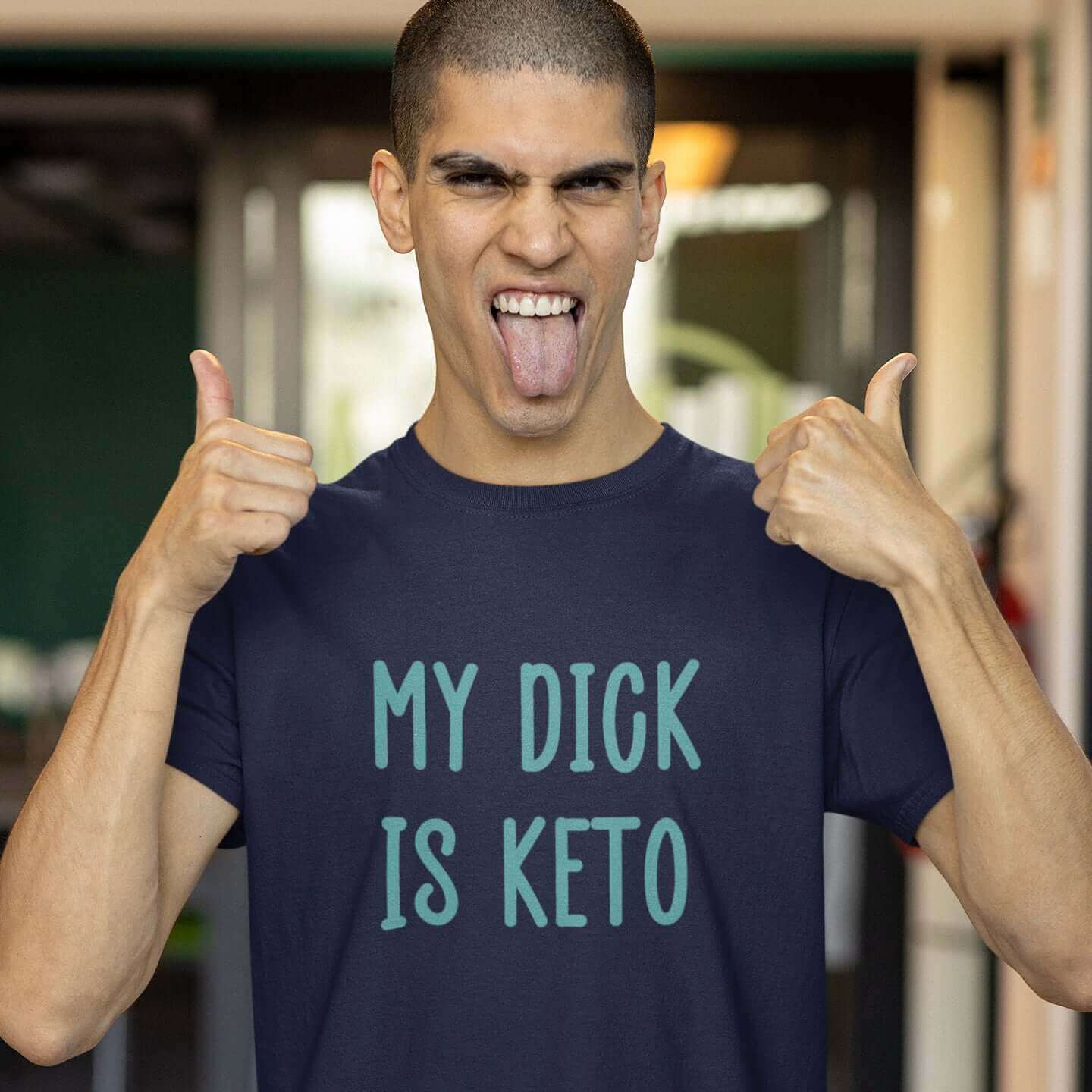 Smiling man wearing navy blue t-shirt with the phrase My dick is keto printed on the front in turquoise font.