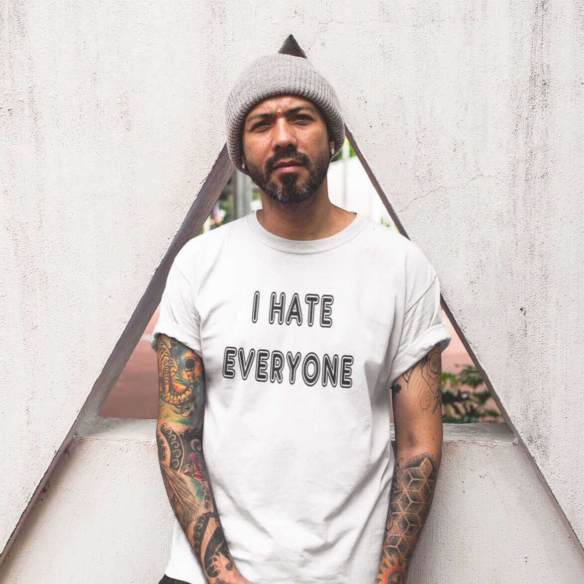 Man leaning against wall wearing white t-shirt with the words I hate everyone printed on the front.
