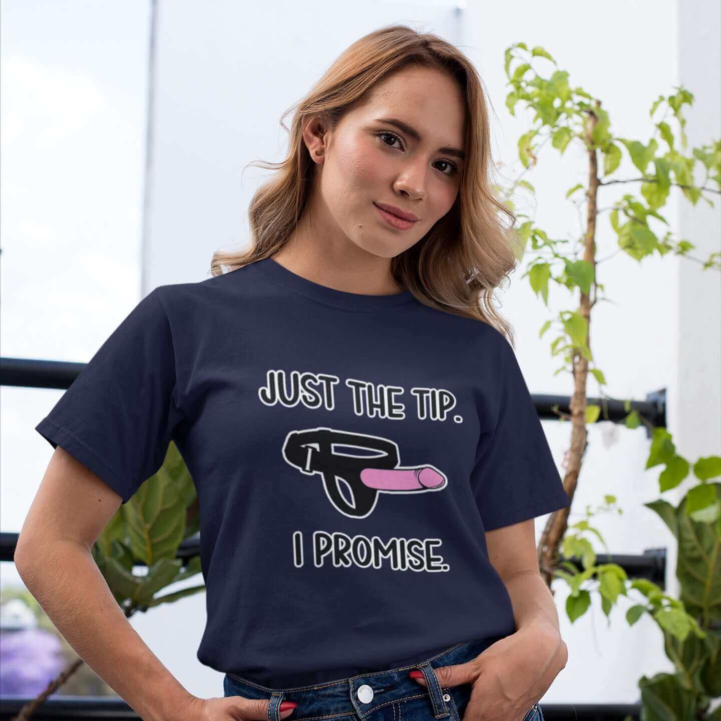 Woman wearing navy blue t-shirt that has an image of a strap-on dildo and the words Just the tip, I promise printed on the front. The graphics are pink, black and white.