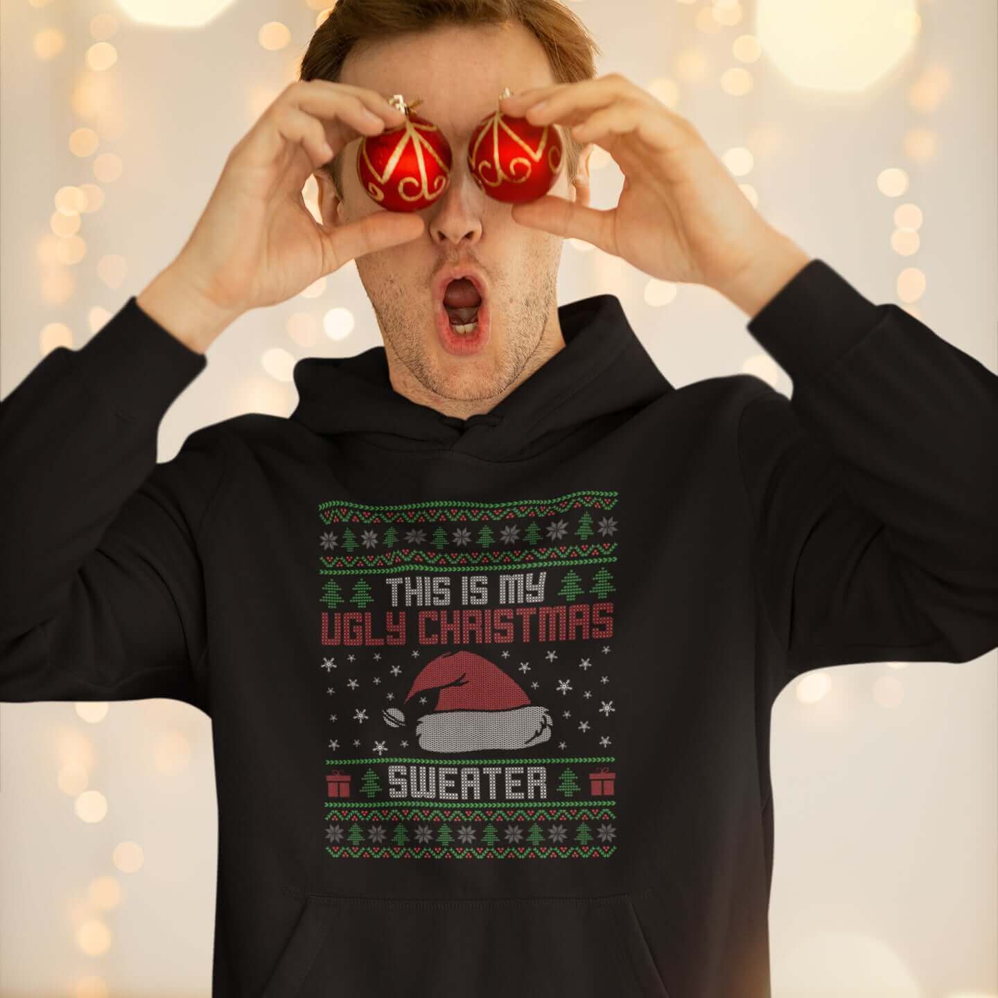 Man in festive holiday setting wearing black hooded sweatshirt with the words This is my ugly Christmas sweater printed on the front. 