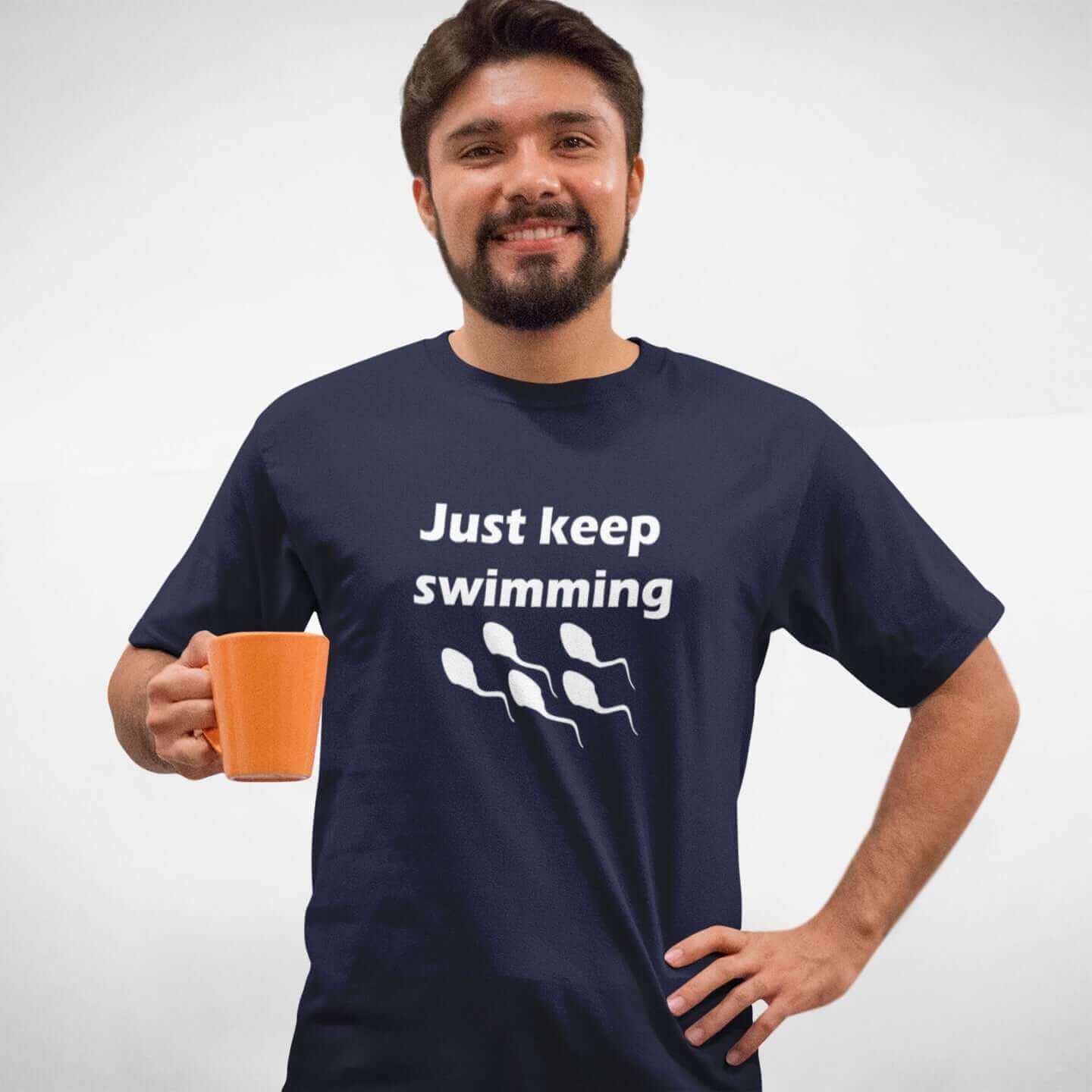 Man wearing a navy blue t-shirt with the phrase Just keep swimming printed on the front. There is an image of some swimming sperm underneath the words.