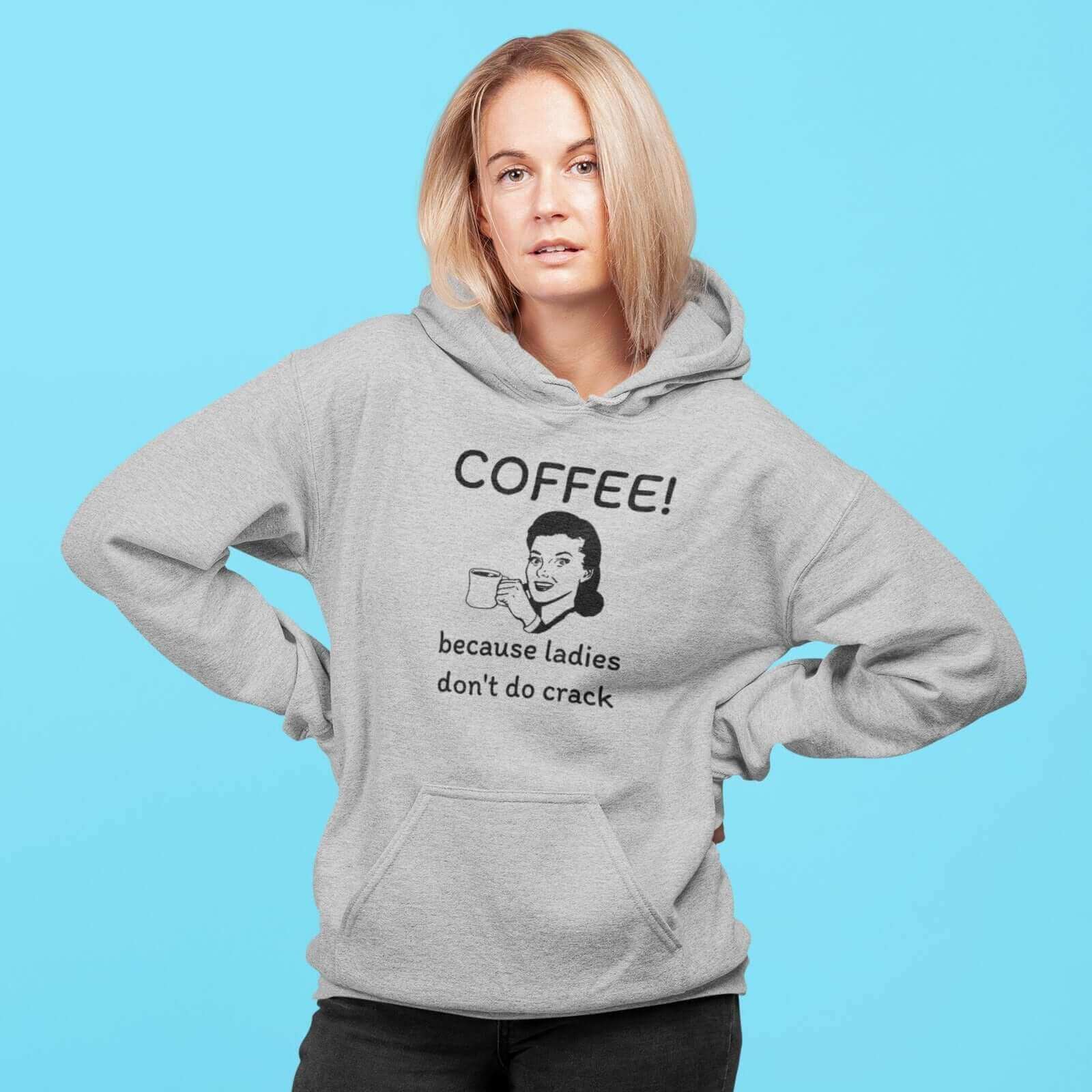 Woman wearing a light grey hoodie sweatshirt with an image of a retro woman holding a coffee mug with the phrase Coffee, because ladies don't do crack printed on the front.