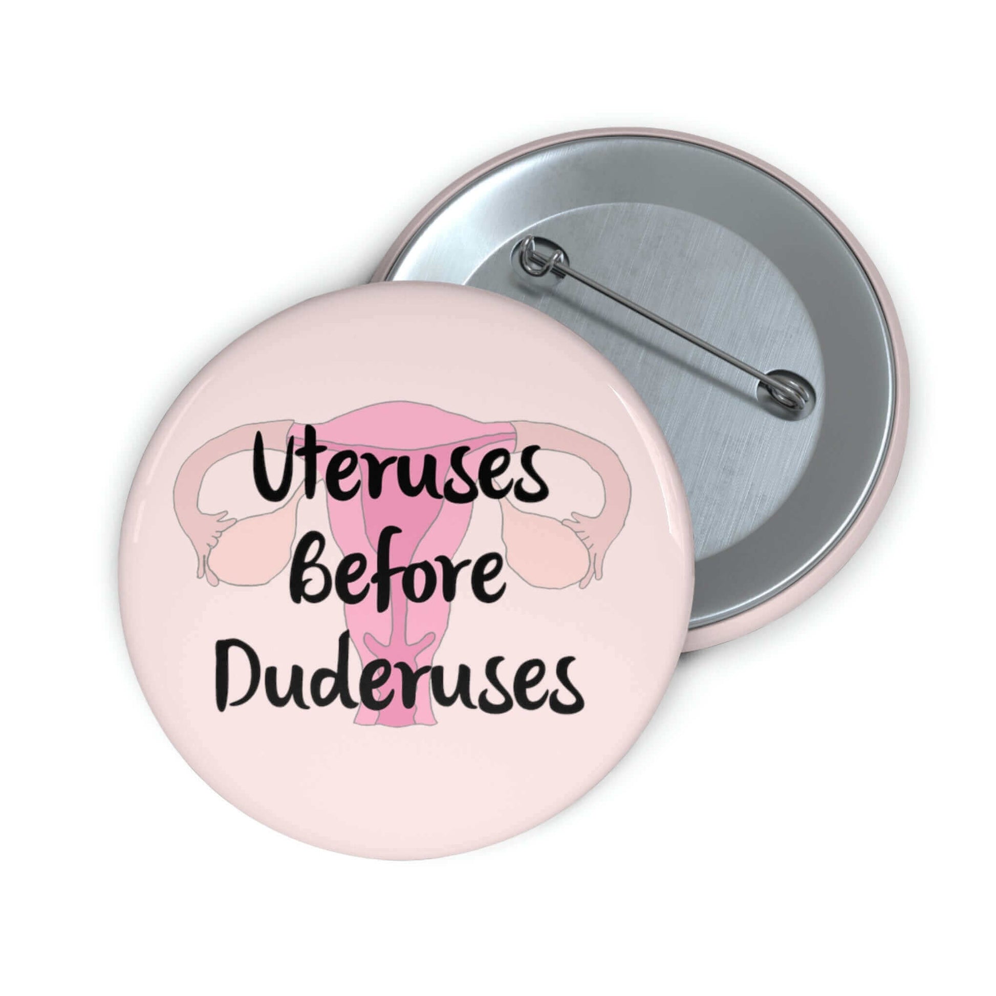 Pink pinback button with image of a uterus and the words Uteruses before duderuses.