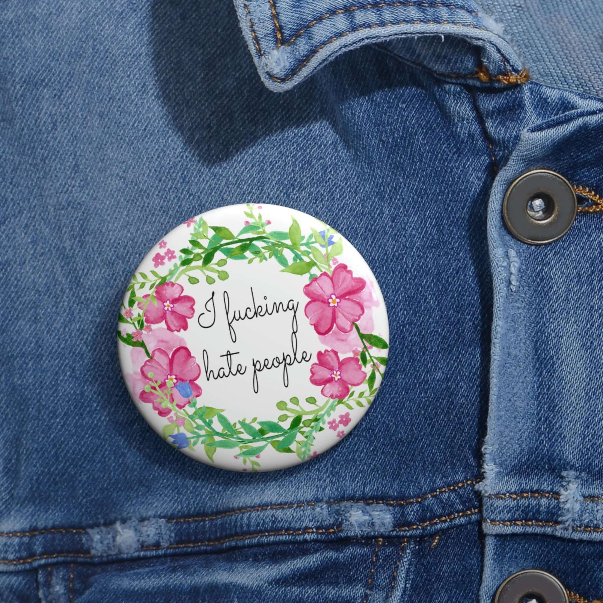 Pinback button with pink and green floral wreath image. The words I fucking hate people are in the center of the wreath.