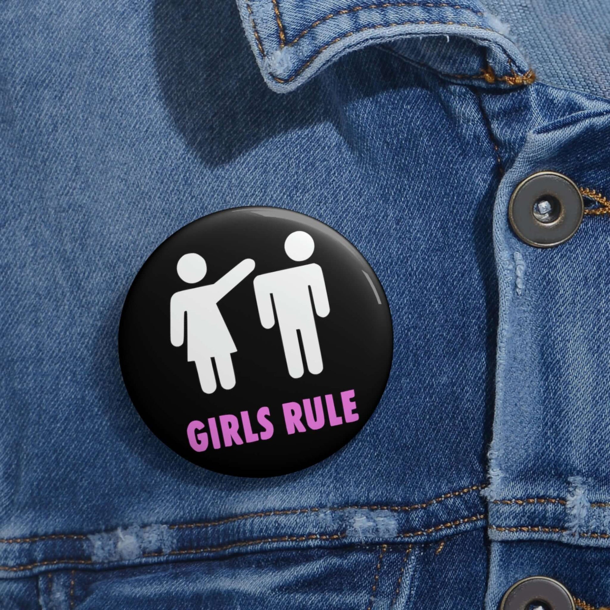 Black pin-back button with white stick figure man and woman. The woman is punching the mans head off and the words Girls rule is printed beneath in hot pink.