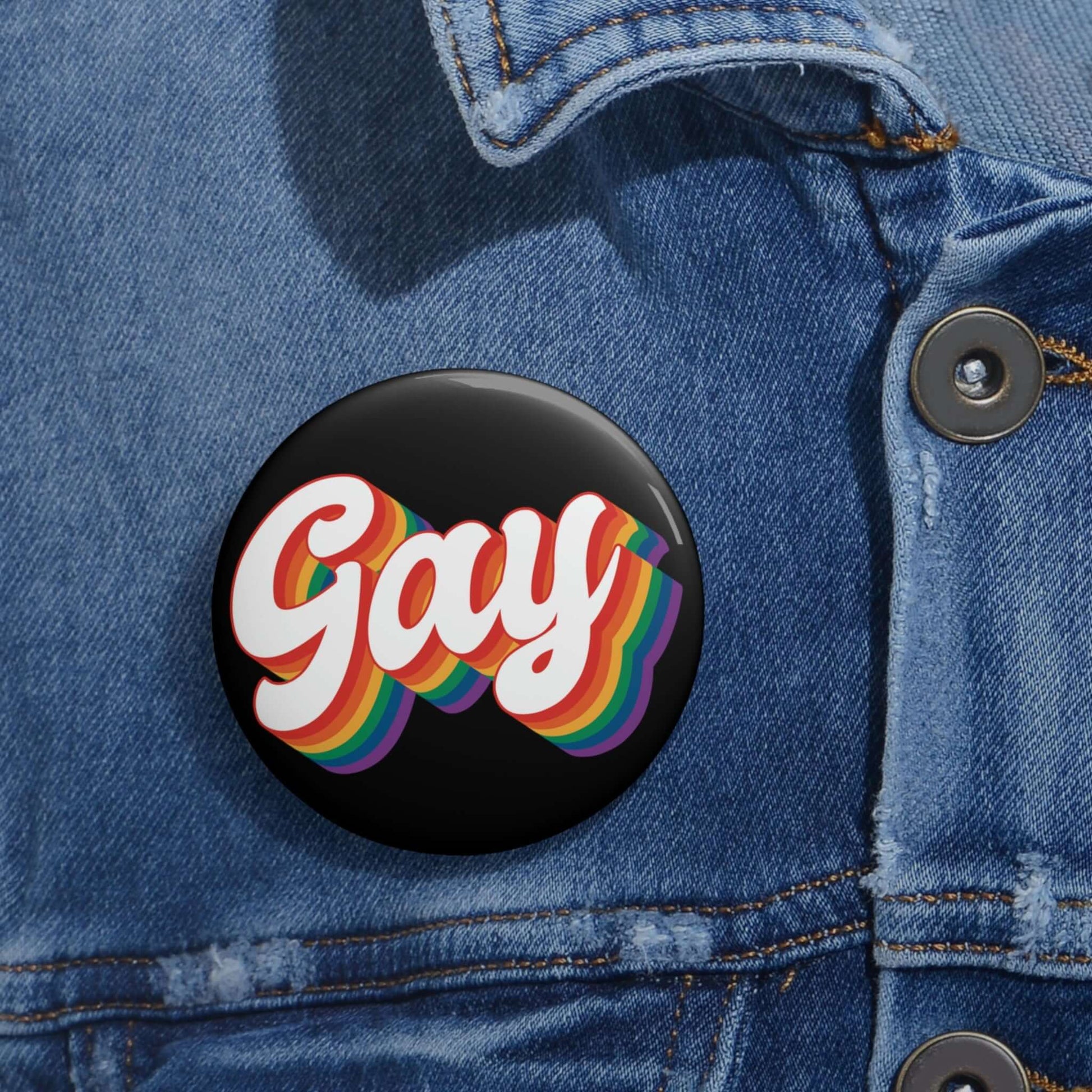 Black pinback button with the word gay in rainbow font.