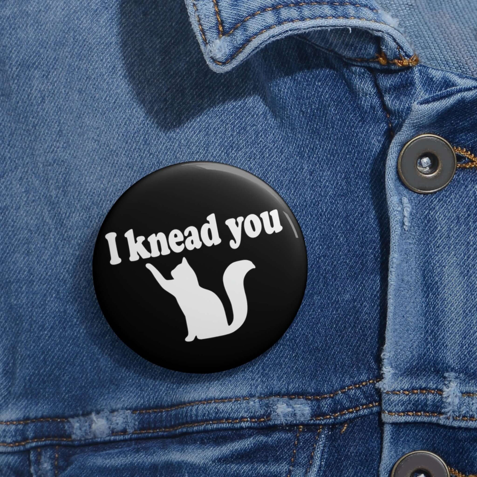 Pin-back button with silhouette of a cat and the words I knead you.