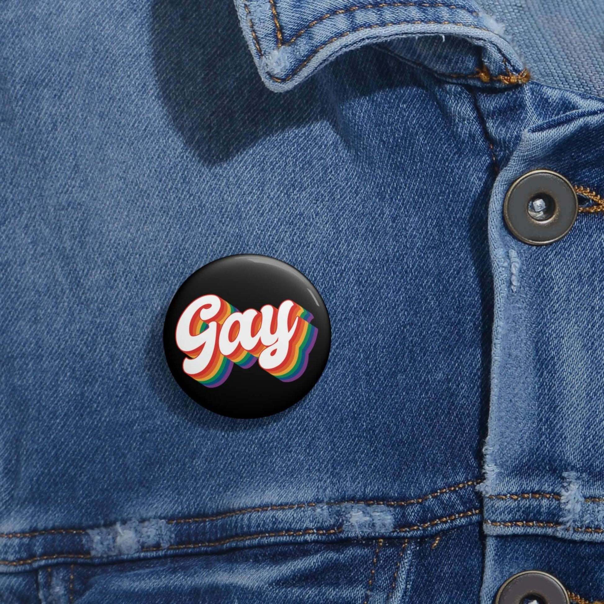 Black pinback button with the word gay in rainbow font.