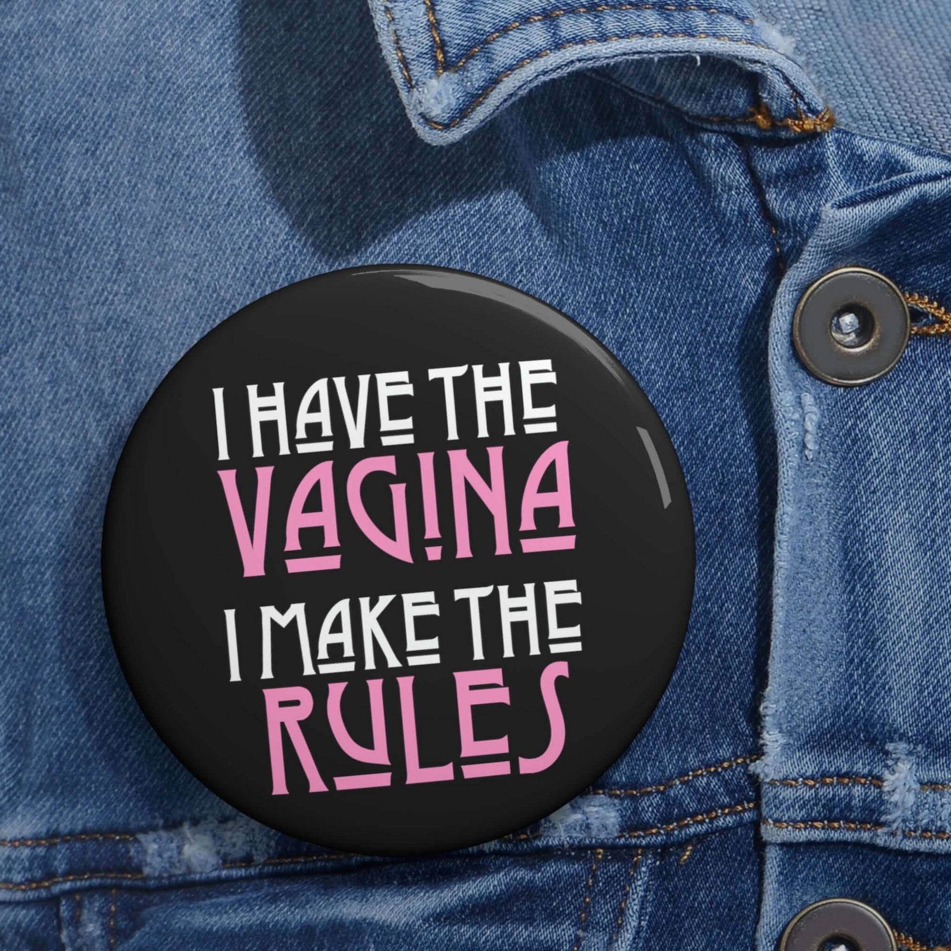 Pinback button that says I have the vagina , I make the rules. The words vagina and rules are pink, the rest of the words are white.