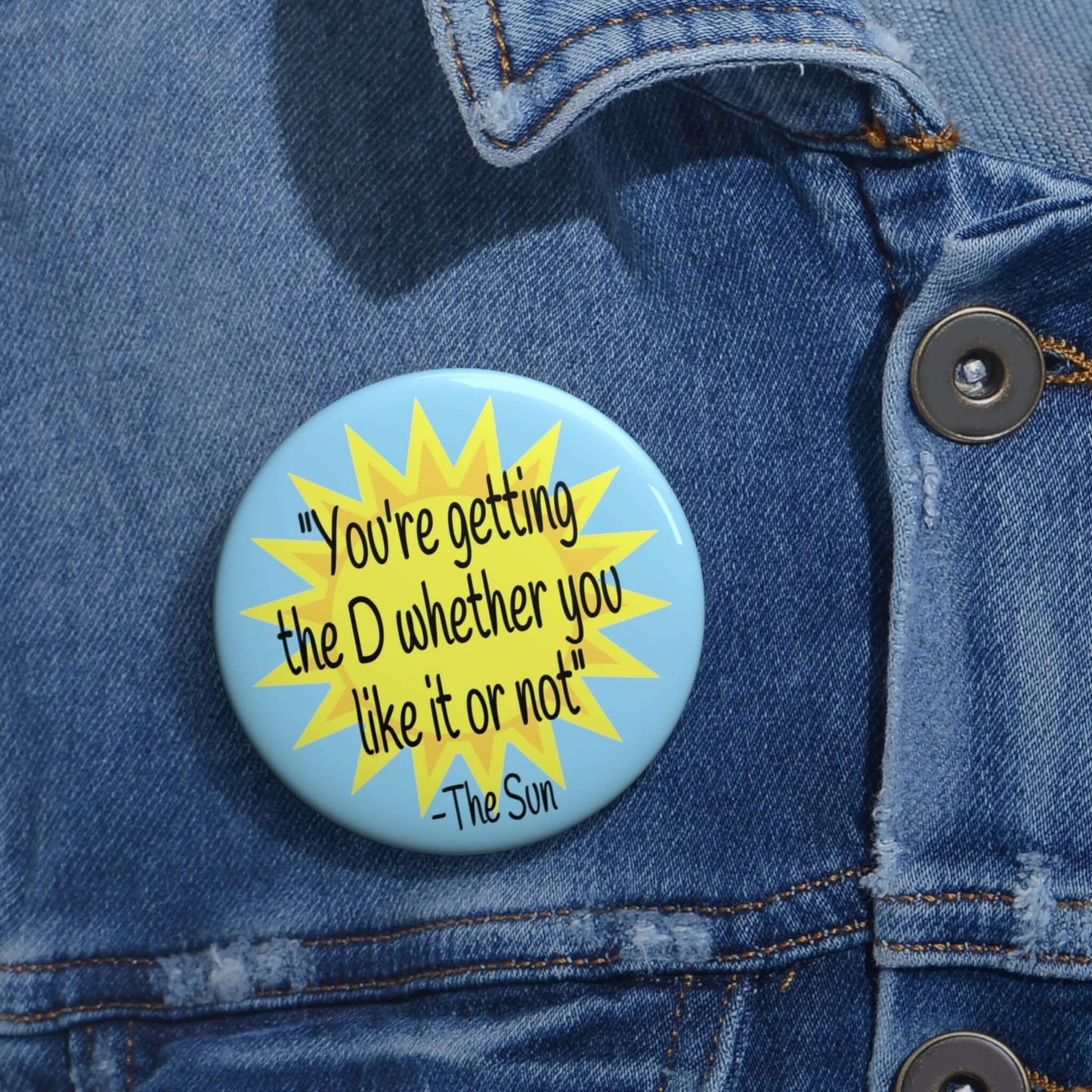 Pinback button with image of the sun and the quote You're getting the D whether you like it or not printed on it.