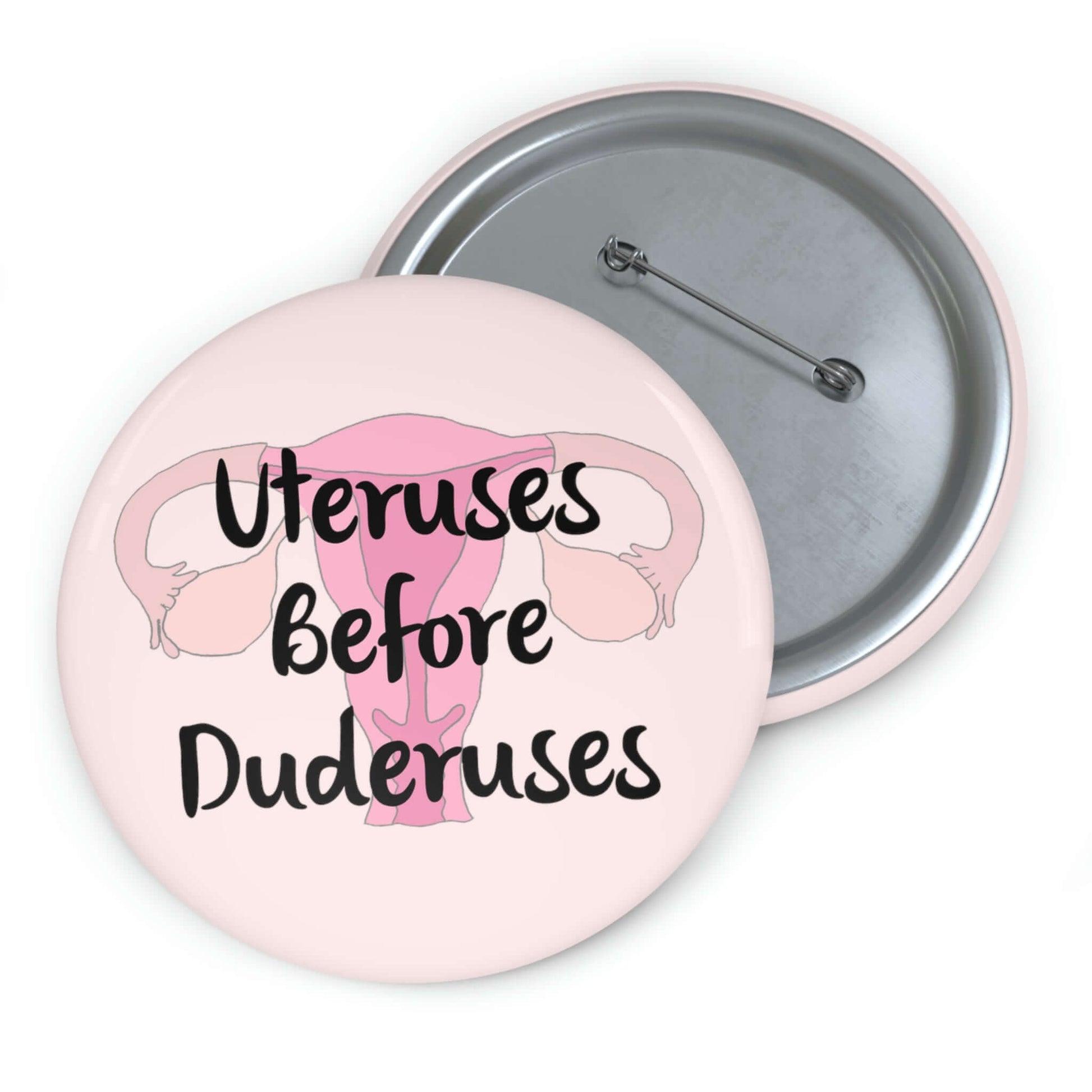 Pink pinback button with image of a uterus and the words Uteruses before duderuses.