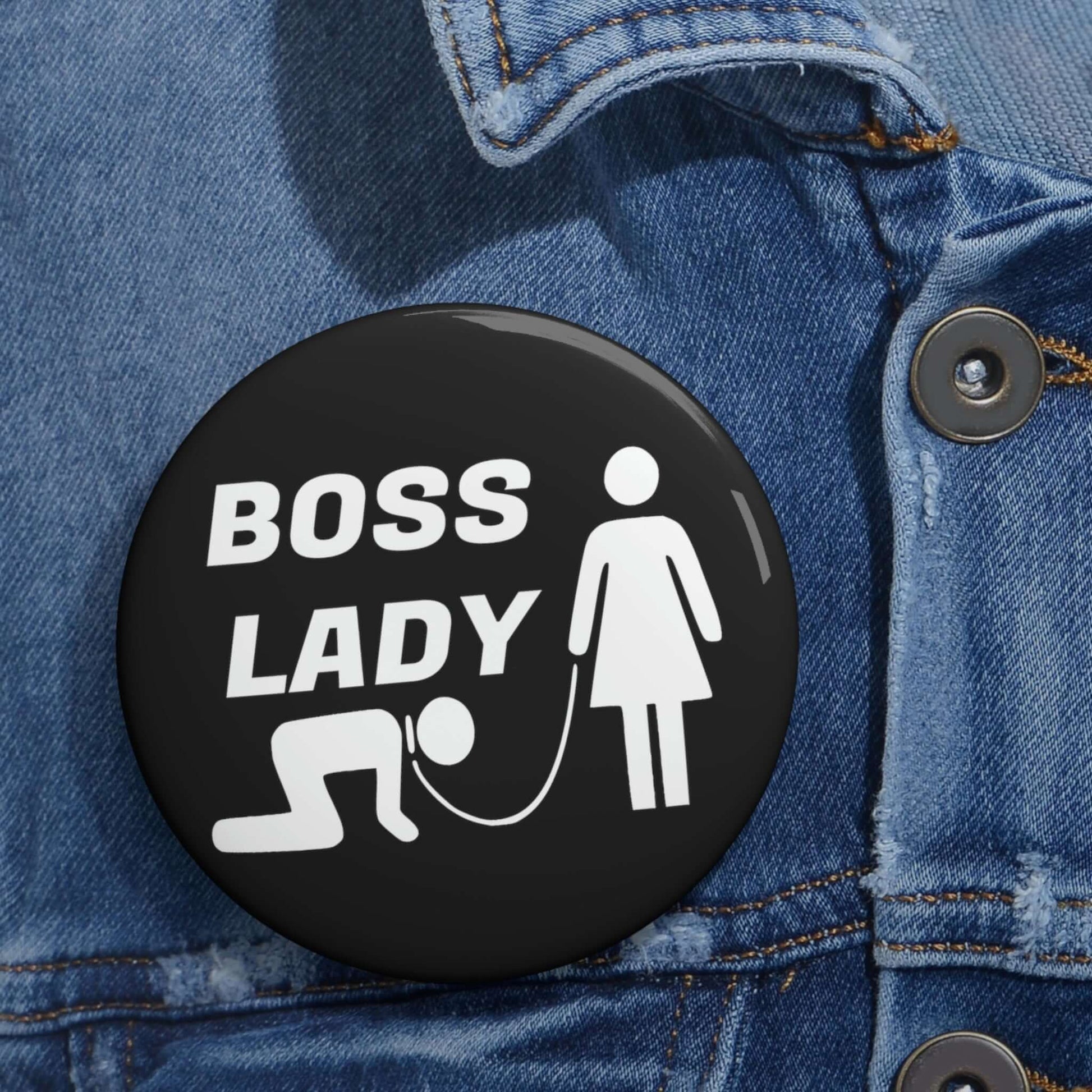 Black pinback button with graphic of collared and leashed man on his hands and knees being led by a woman and the words Boss lady.