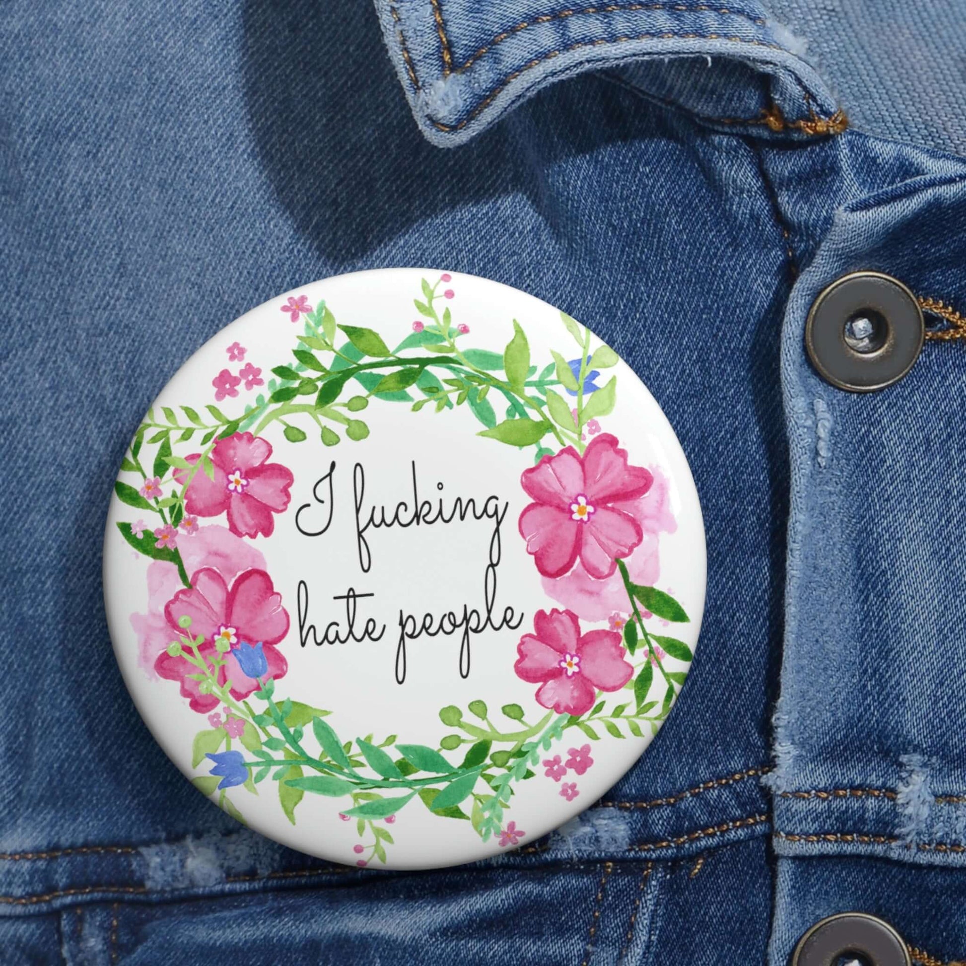 Pinback button with pink and green floral wreath image. The words I fucking hate people are in the center of the wreath.