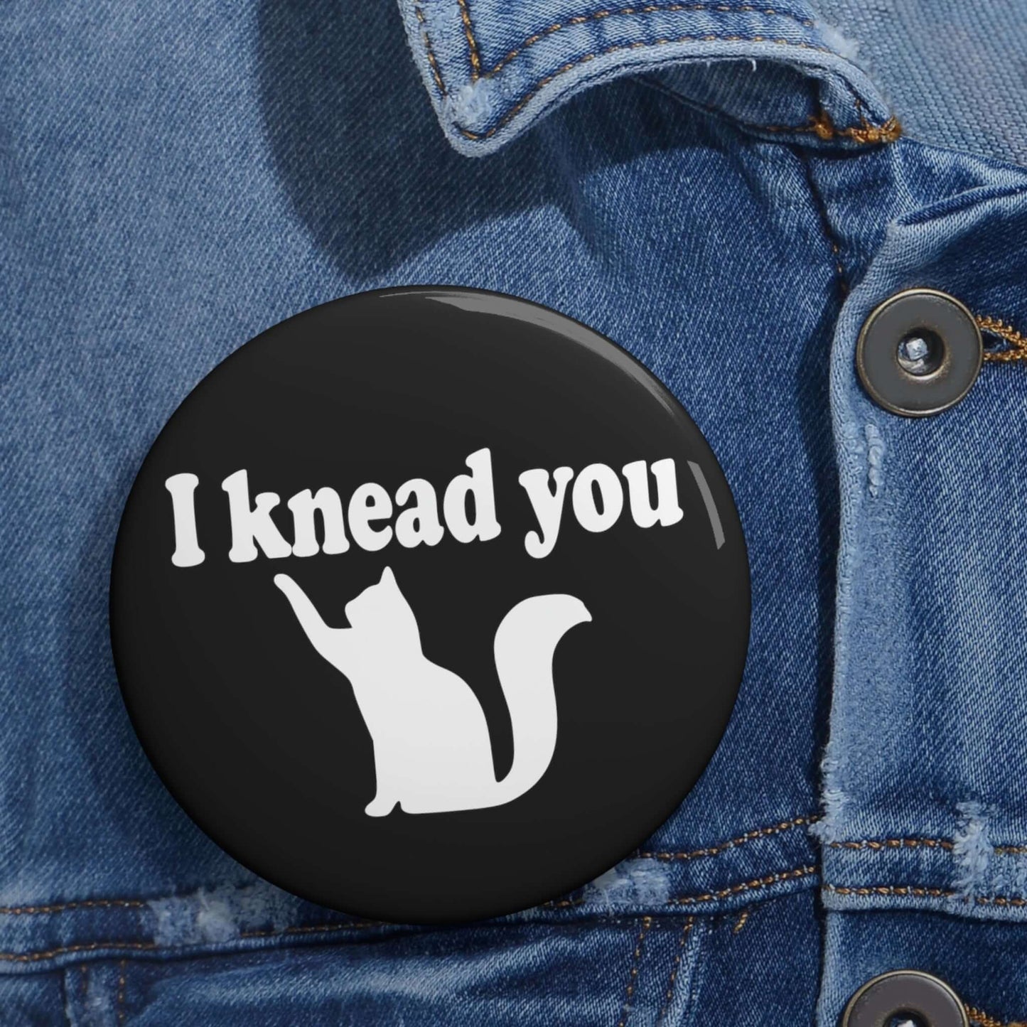 Pin-back button with silhouette of a cat and the words I knead you.