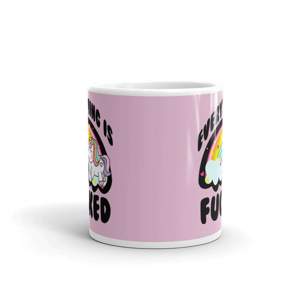 White ceramic coffee mug with a graphic of a kawaii style unicorn and a pastel rainbow with the words Everything is fucked printed on both sides. The background is pink.
