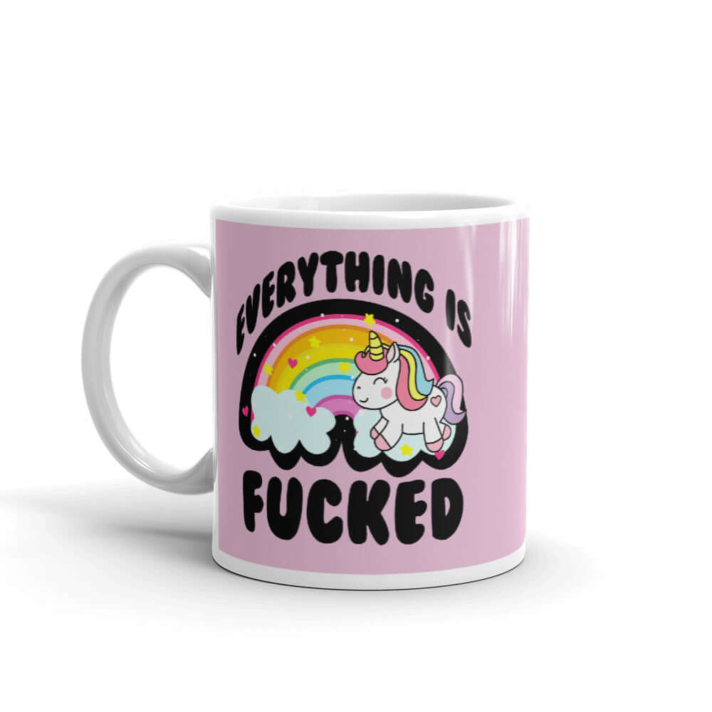 White ceramic coffee mug with a graphic of a kawaii style unicorn and a pastel rainbow with the words Everything is fucked printed on both sides. The background is pink.