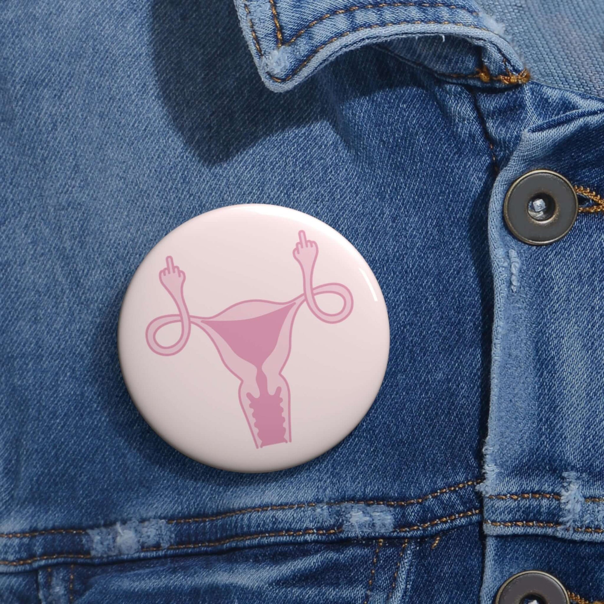 Pink pinback button with image of a uterus flipping the middle finger. 