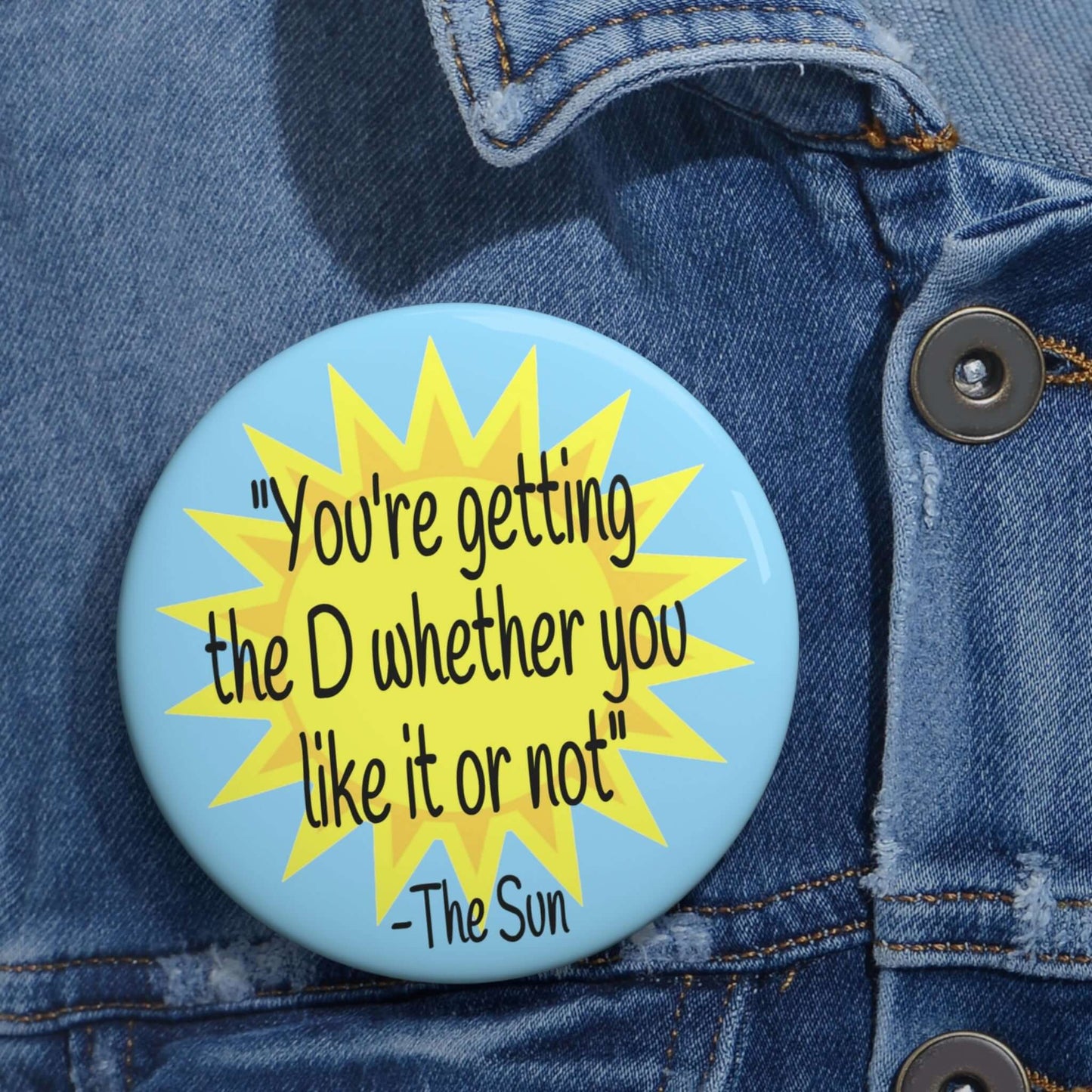 Pinback button with image of the sun and the quote You're getting the D whether you like it or not printed on it.