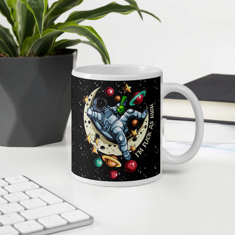 White ceramic mug with graphic of an astronaut sitting on the moon while smoking a bong with the words I'm fuck as high printed on both sides of the mug. The mug has a black speckled background.