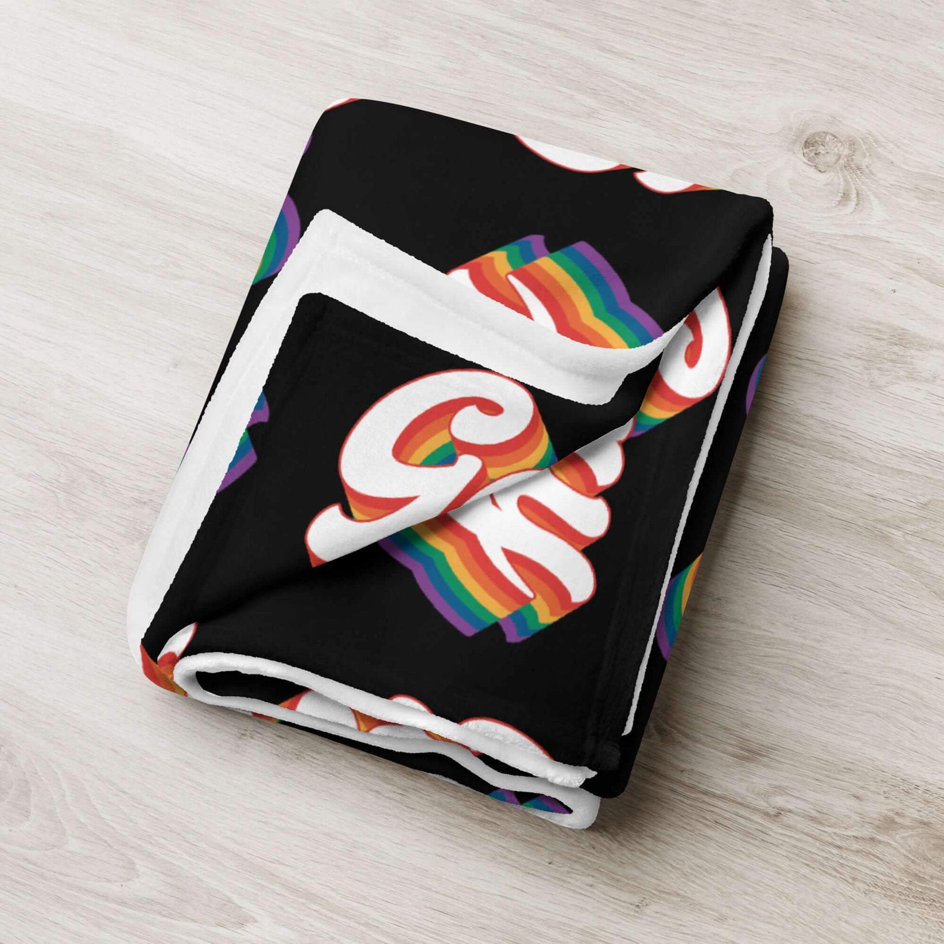 Black throw blanket with the word gay in rainbow font printed all over.