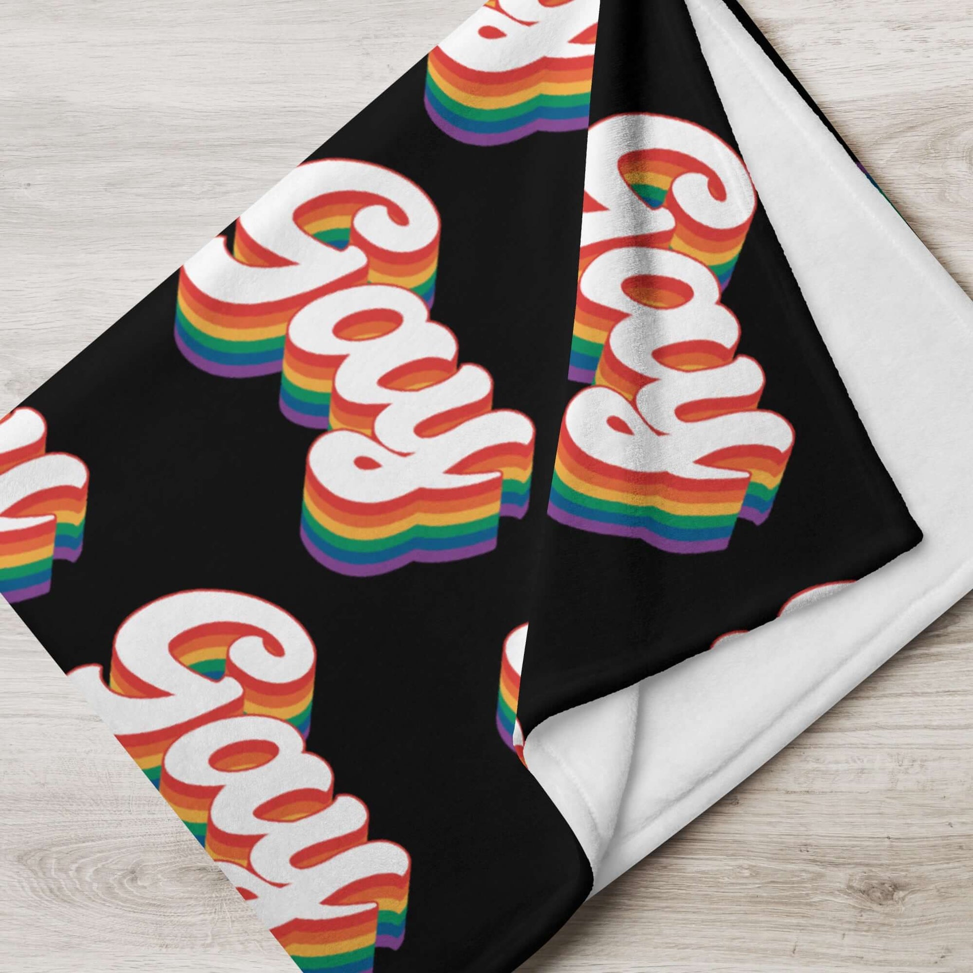 Black throw blanket with the word gay in rainbow font printed all over.