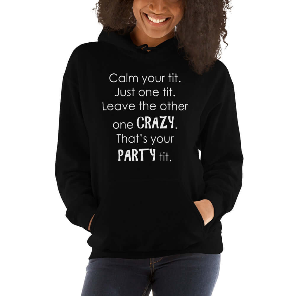 Woman wearing a black hoodie sweatshirt with the funny phrase Calm your tit, just one tit. Leave the other one crazy, that's your party tit printed on the front.