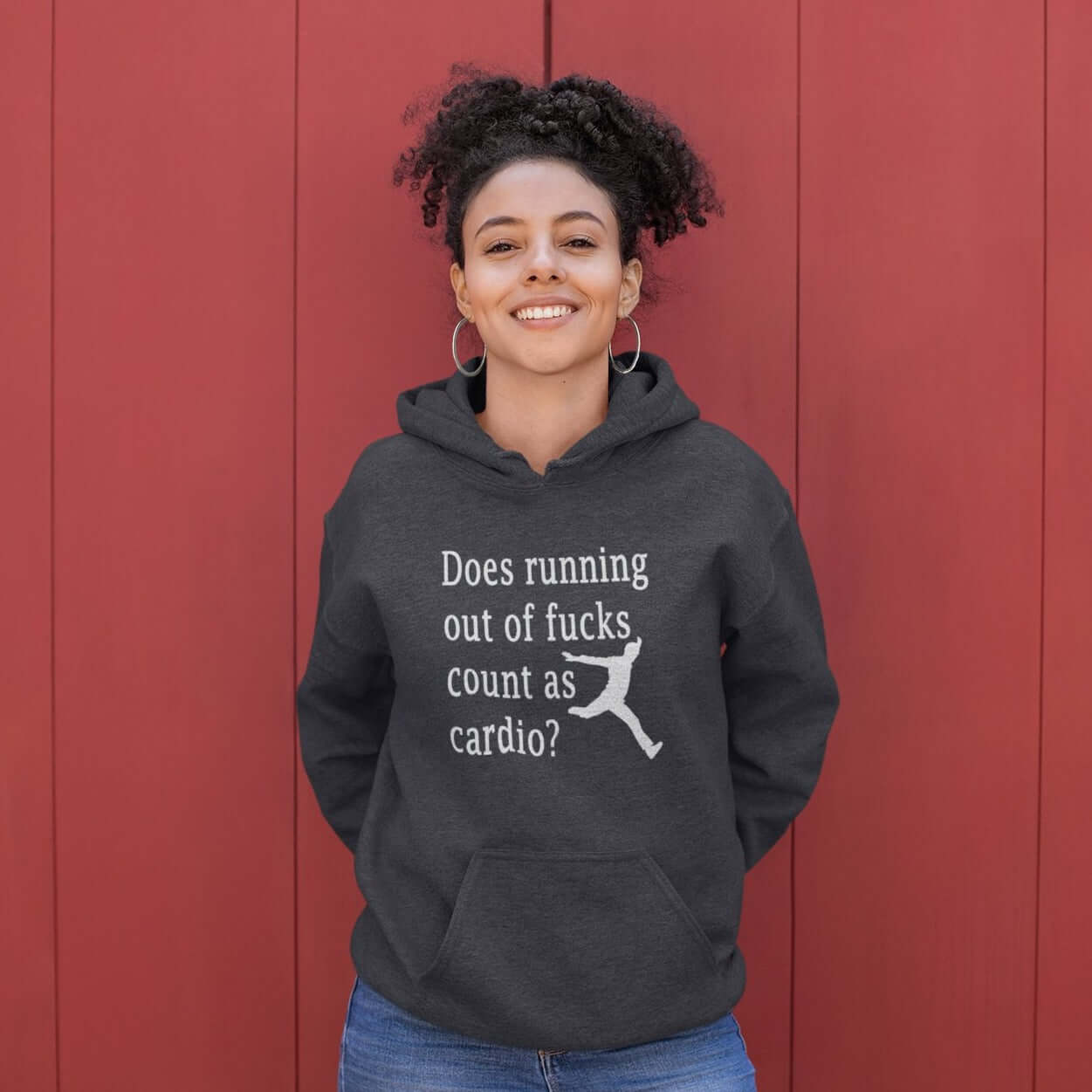 Woman wearing a dark grey hoodie sweatshirt with a silhouette image of a running person with the phrase Does running out of fucks count as cardio question mark printed on the front.