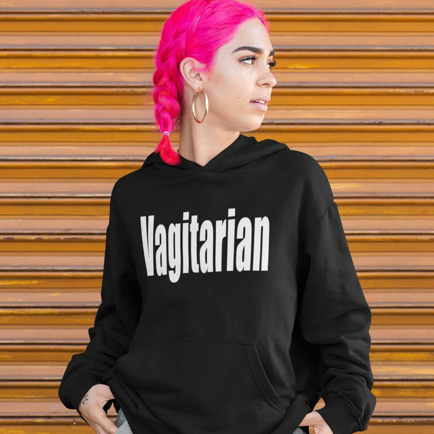 Woman with bright pink hair wearing a black hoodie sweatshirt with the word Vagitarian printed on the front.