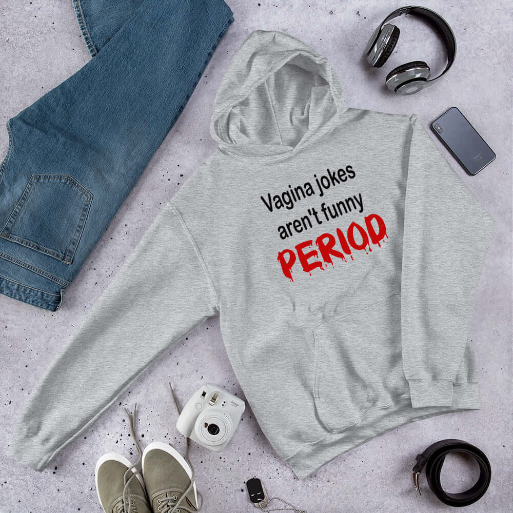 Light grey hoodie sweatshirt with the crude phrase Vagina jokes aren't funny...period. The word period is in a red drippy font. The graphics are printed on the front of the hoodie.