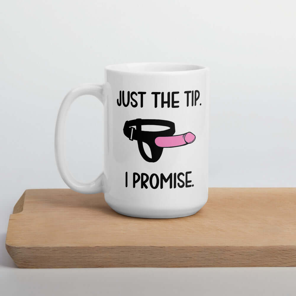 White ceramic coffee mug that has an image of a strap-on dildo and the words Just the tip, I promise printed on both sides. The graphics are pink, black and white.