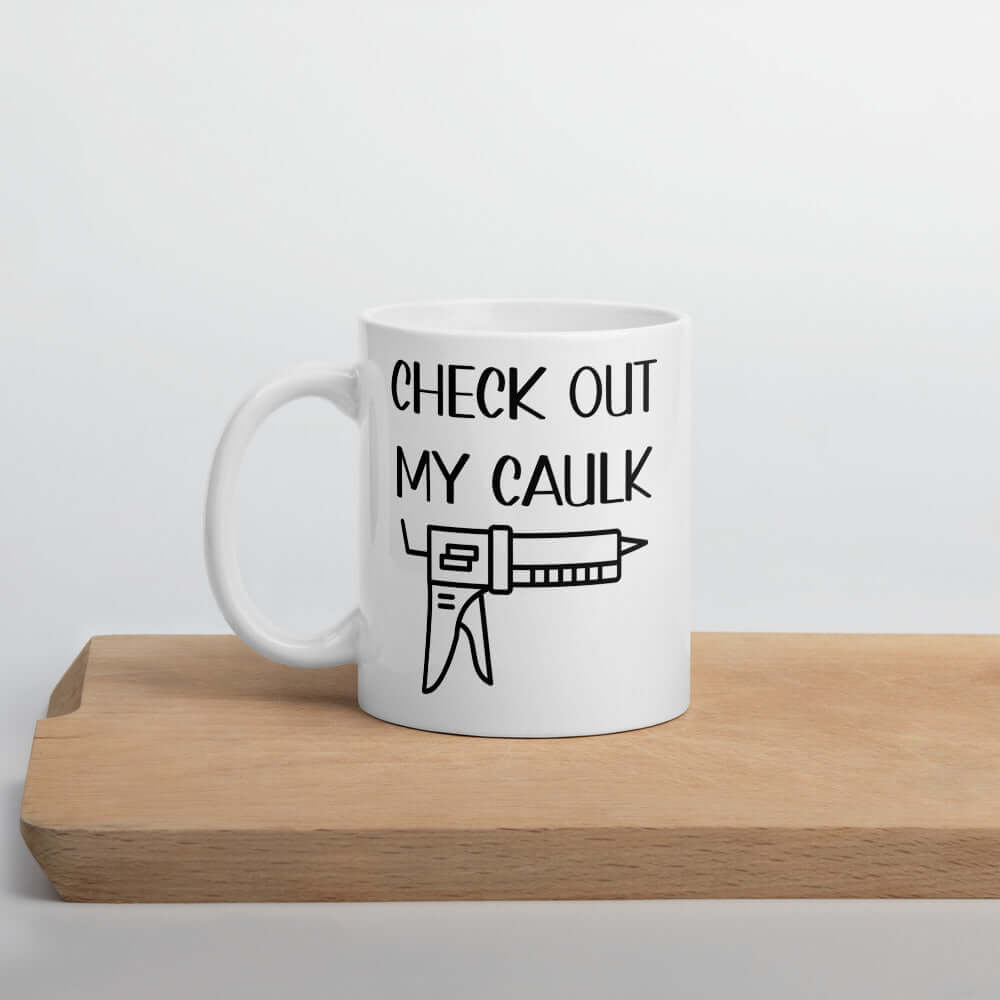 White ceramic coffee mug with the pun phrase Check out my caulk with a line drawing image of a caulking gun printed on both sides.