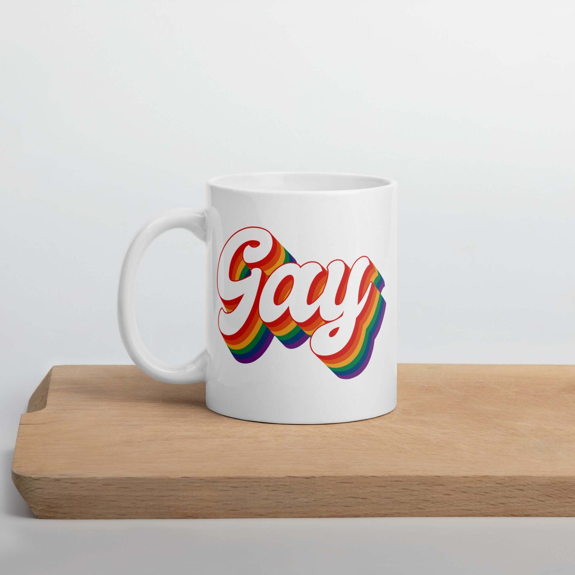 White ceramic mug with the word Gay printed on both sides. The word gay is outlined in rainbow.