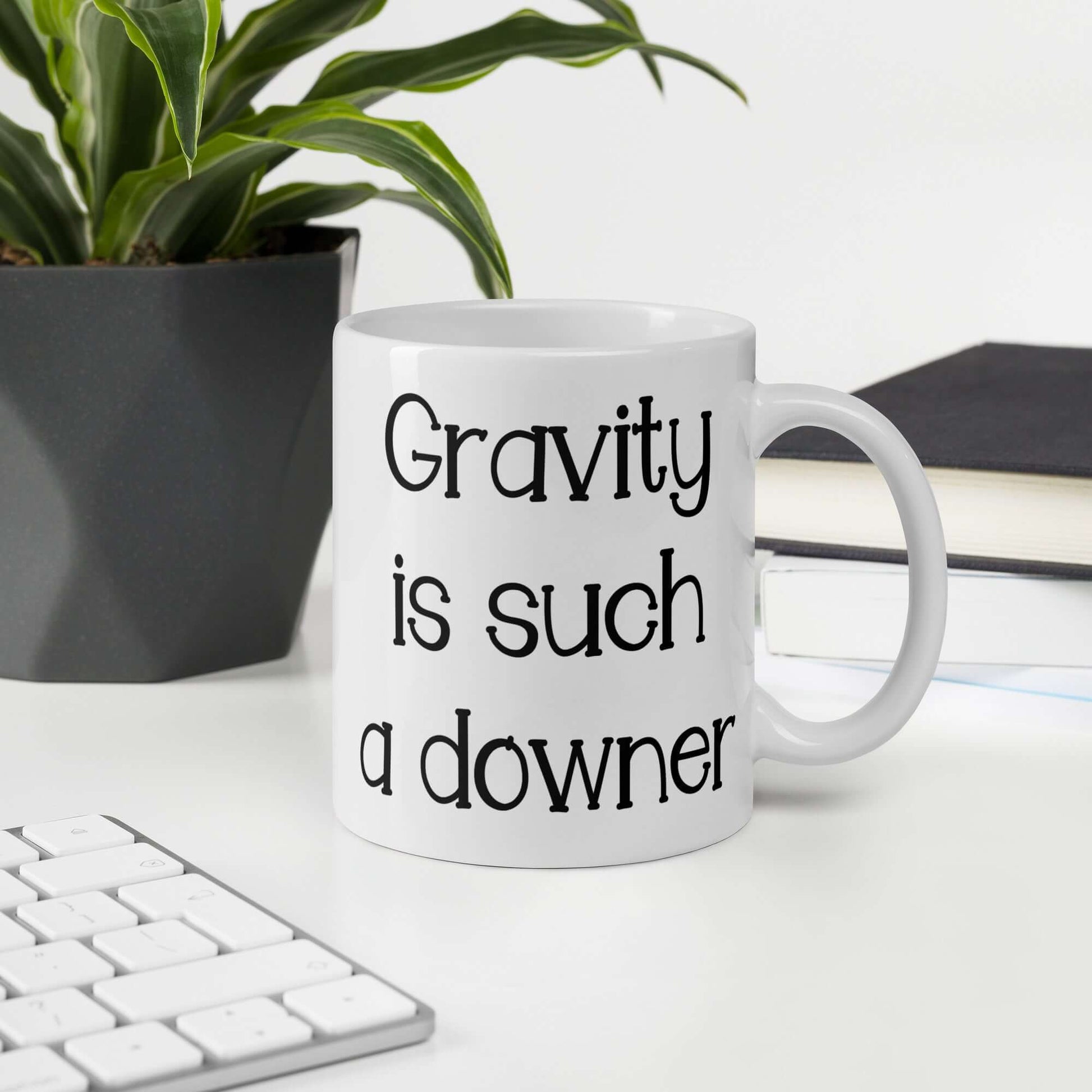 White ceramic coffee mug with the words Gravity is such a downer printed on both sides.