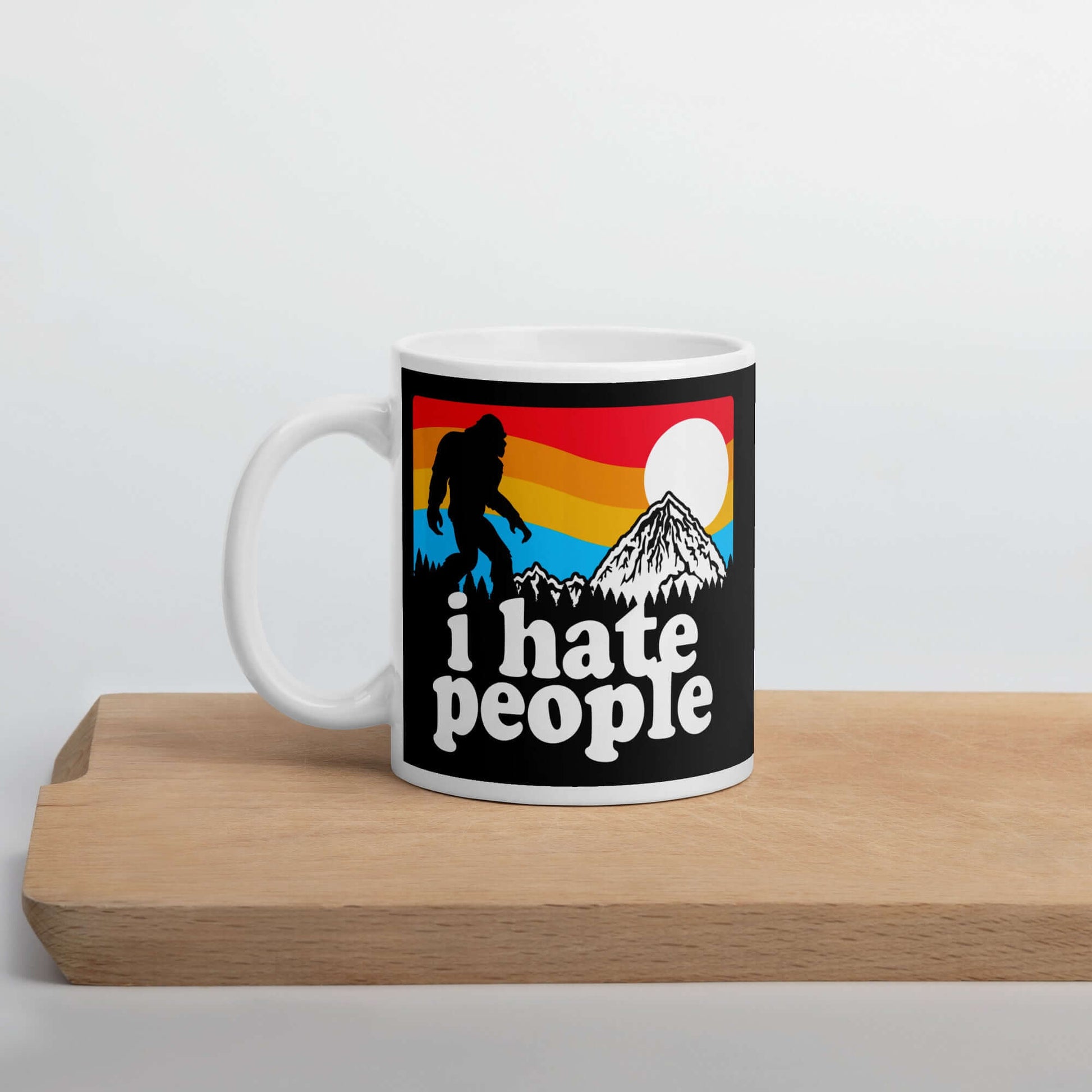 White coffee mug with graphic of Bigfoot walking into the sunset with the words I hate people printed on both sides. 