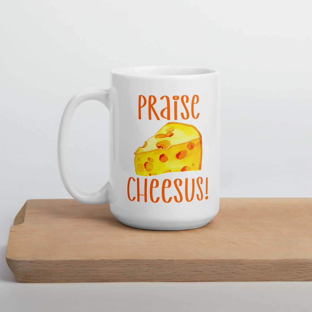 White ceramic coffee mug with funny graphics of a piece of swiss cheese and the words Praise Cheesus printed on both sides of the mug in yellow and orange.